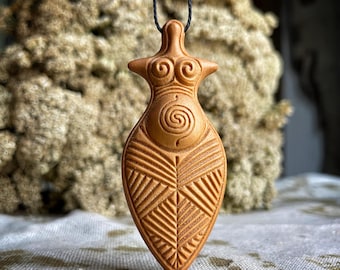 May include: A tan-coloured pendant necklace depicting a stylised female figure. The pendant has a carved design with geometric patterns and a spiral. The necklace hangs from a black cord, showcasing a unique, handcrafted design.