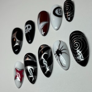 K&ouml;nnte beinhalten: Ein Set aus zehn k&uuml;nstlichen N&auml;geln mit verschiedenen Designs. Die N&auml;gel weisen eine Mischung aus schwarzen, wei&szlig;en, silbernen und roten Farben auf. Designs umfassen einen Totenkopf, eine Spinne und abstrakte Muster. Die N&auml;gel sind oval geformt.