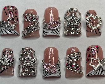 May include: A set of ten artificial nails with various designs. The nails feature a nude base with accents like zebra stripes, leopard print, and rhinestones. Some nails have star, heart, or lip-shaped embellishments.