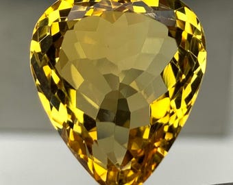 May include: A faceted, pear-shaped gemstone with a vibrant yellow hue. The gem is held by a pair of tweezers, showcasing its intricate cut and brilliance. The stone's facets reflect light, creating a dazzling display of color and sparkle.
