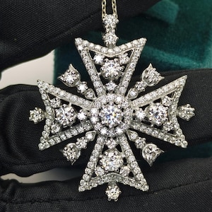 May include: A diamond pendant necklace with an elaborate cross design. The pendant is set with many small diamonds, and larger stones at the center and cross points. The necklace chain is a delicate gold colour.