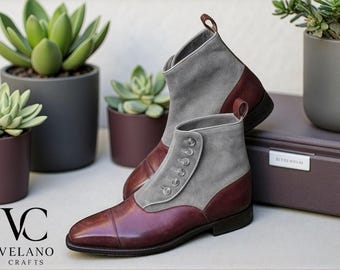 May include: A pair of stylish ankle boots with a gray suede upper and burgundy leather accents. The boots feature a button closure and a pull tab. The boots are displayed with potted succulents, showcasing a sophisticated aesthetic.