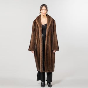 May include: A full-length brown fur coat with a wide collar and long sleeves. The coat is buttoned up and worn over a black top and pants. The coat has a luxurious appearance and is suitable for cold weather.