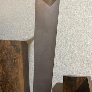 K&ouml;nnte beinhalten: Eine hohe, metallische, graue Turbinen-Statorschaufel mit einem glatten, sich verj&uuml;ngenden vertikalen Design. Die Schaufel ist auf einem rechteckigen Holzsockel montiert, der die Gravur Titanium Stator Blade tr&auml;gt und industriell wirkt.
