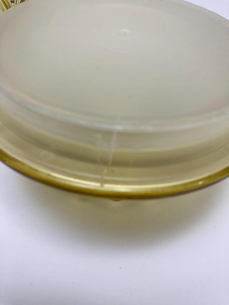 May include: A clear, round, plastic container lid with a slightly frosted appearance. The lid has a yellow-tinted rim and a slightly domed center. The container is likely for food storage.