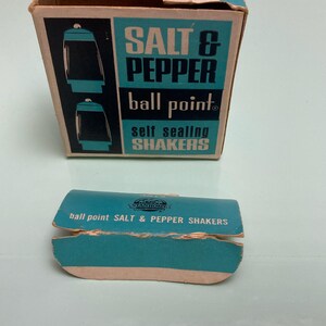 May include: Vintage salt and pepper shaker set in original packaging. The box is brown with a teal and black label that reads "SALT & PEPPER ball point self sealing SHAKERS." A separate teal lid is also visible.