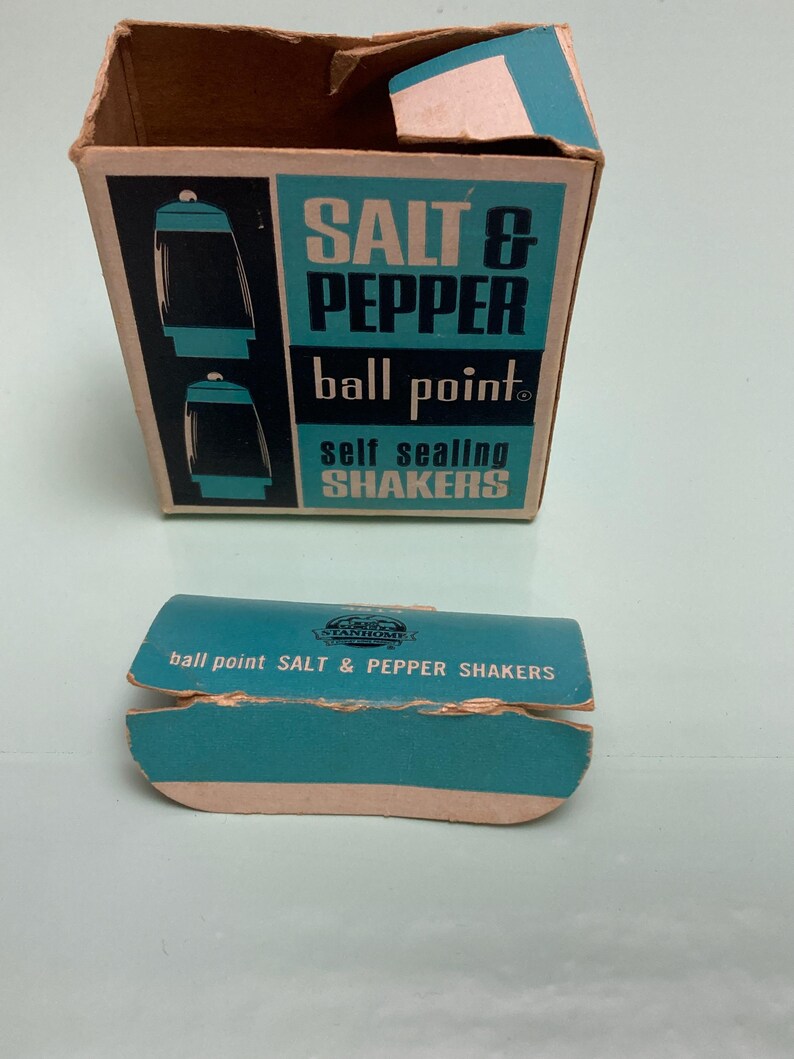 May include: Vintage salt and pepper shaker set in original packaging. The box is brown with a teal and black label that reads "SALT & PEPPER ball point self sealing SHAKERS." A separate teal lid is also visible.