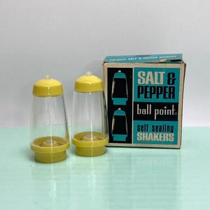 May include: Two clear plastic salt and pepper shakers with yellow lids and bases. The shakers are next to a box that reads "SALT & PEPPER ball point self sealing SHAKERS" in teal and black.