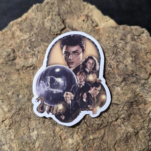 May include: A die-cut sticker featuring a collage of characters from the Harry Potter film series. The sticker showcases Harry Potter, Hermione Granger, Ron Weasley, and other characters, with a dark background and a snake.