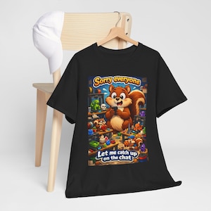 May include: Black t-shirt featuring a cartoon squirrel holding a phone, surrounded by toys and shelves. The shirt has the text "Sorry everyone" and "Let me catch up on the chat". The design is colorful and playful, suitable for casual wear.