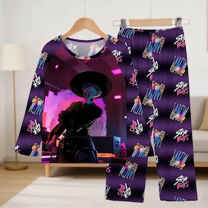 May include: Purple pajama set featuring a long-sleeved top and pants. The top displays a stage performance graphic, while the pants have a repeating pattern of a group of people and the text "Six Boys".