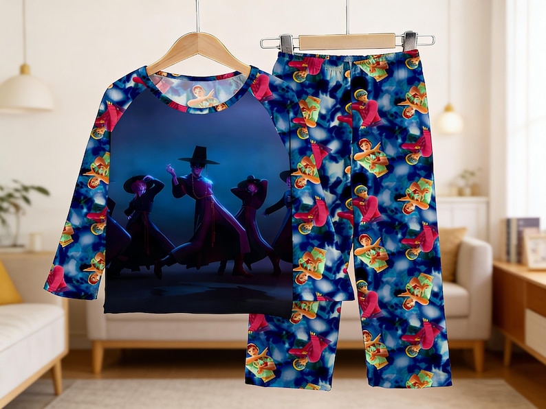 May include: A two-piece pajama set featuring a long-sleeved top and pants. The top has a dark blue background with a graphic of figures in traditional Korean attire. The pants have a repeating pattern of figures in red and green on a blue background.