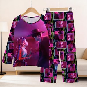 May include: A pajama set featuring a long-sleeved top and pants. The top displays a vibrant illustration of two figures in a romantic scene, while the pants are patterned with repeating images of the same figures. The color palette includes shades of pink, purple, and black.