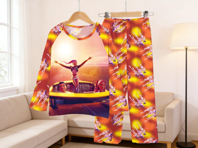 May include: A two-piece pajama set featuring a long-sleeved top and pants. The top has a graphic of a woman with her arms raised in a car, with a sunset background. The pants and sleeves have a repeating pattern of a woman in a car.