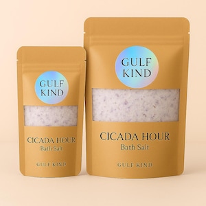 Peut inclure: Deux sachets en papier brun contenant des sels de bain. Les sachets ont une fenêtre transparente montrant le sel à l'intérieur. Chaque sachet porte un autocollant holographique "GULF KIND". Le texte "CICADA HOUR Bath Salt" est imprimé.