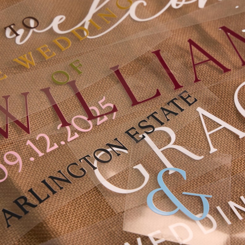 May include: Close-up of several clear, transparent sheets with wedding-themed text in various colors. The text includes names, dates, and locations, such as "William" and "Arlington Estate". The background is a textured, tan fabric.