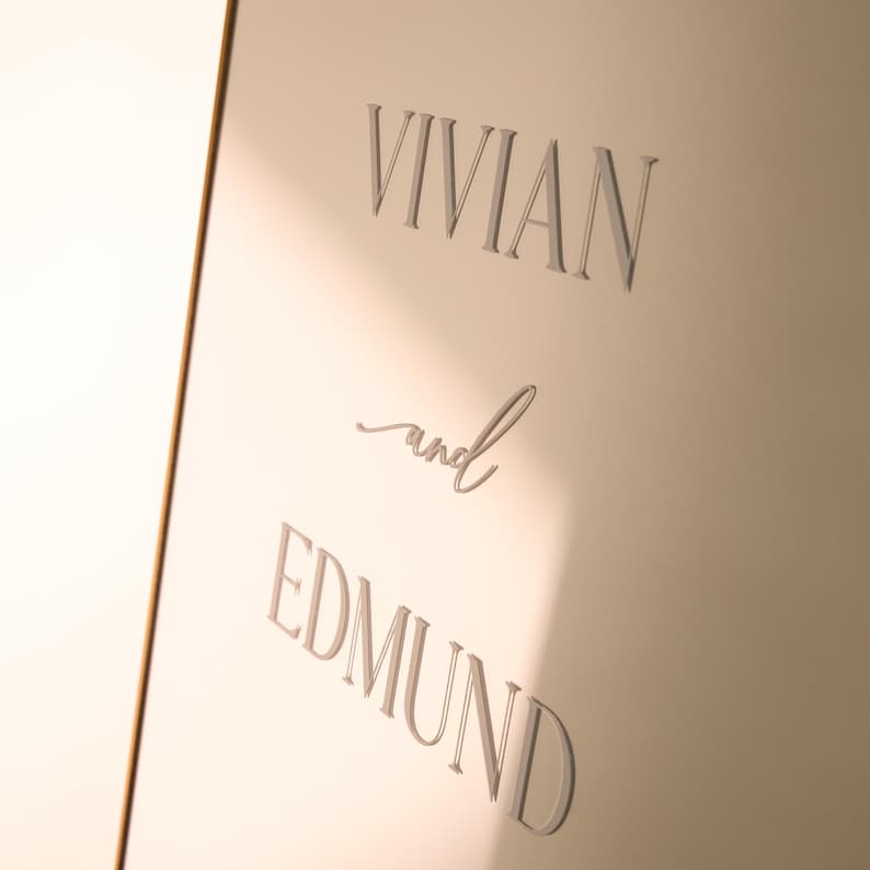 May include: A light-colored surface with the names "Vivian" and "Edmund" in elegant, raised lettering. The word "and" is written in a cursive script between the names. The overall design is simple and sophisticated.