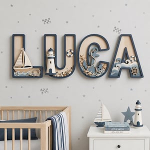 Könnte beinhalten: Große hölzerne Wandbuchstaben, die den Namen LUCA in einem nautischen Thema bilden. Jeder Buchstabe hat einen dunkelblauen Rahmen mit hellem Holz im Inneren. Dekorationen umfassen ein Segelboot, einen Leuchtturm, einen Rettungsring, einen Anker und Wellen.