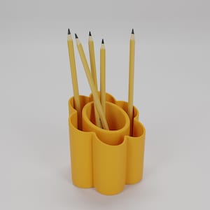 May include: A yellow pencil holder with a unique, curved design, holding several yellow pencils with black tips. The pencils are arranged in the holder, creating a functional and stylish desk accessory.