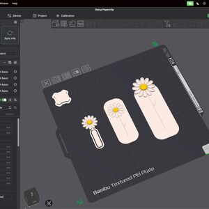 May include: A digital interface for Bambu Studio software displaying a 3D print project titled Daisy Paperslip. The screen shows a virtual build plate with three daisy-themed designs in white, yellow, and light pink, alongside printer settings.