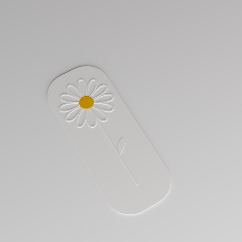 May include: A white rectangular bookmark with rounded corners featuring an embossed daisy flower design. The flower has a bright yellow centre and white petals, with a single embossed stem and leaf extending downwards on the white surface.