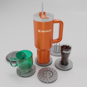 Peut inclure: Une tasse de voyage Stanley orange avec un couvercle et une poignée blancs, une tasse en verre vert et un verre Coca-Cola avec de la glace. Tous les articles sont sur des dessous de verre gris qui ressemblent à des rotors de frein de voiture.