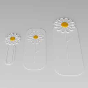 May include: Three white bookmarks of varying lengths, each featuring a raised daisy design with a yellow centre. The smallest bookmark has an open oval base, while the two larger bookmarks are solid rectangular shapes with rounded corners.