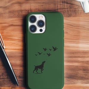 Może przedstawiać: Zielone etui na telefon z czarną sylwetką psa patrzącego w górę na stado ptaków. Etui ma matowe wykończenie i jest przeznaczone do smartfona. Projekt to prosta ilustracja.