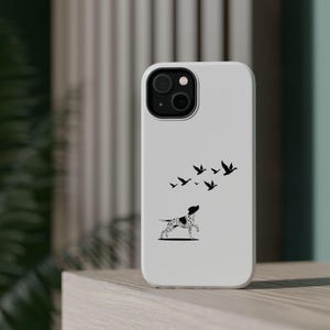 May include: A white phone case featuring a black and white illustration of a dog with black spots looking up at a flock of birds. The case has a camera cutout and is on a wooden surface.