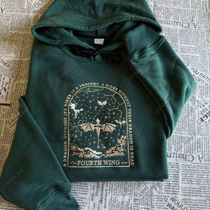 Op de afbeelding: Donkergroene hoodie met een trekkoord in de capuchon. De voorkant heeft een geborduurd ontwerp met een draak, sterren en de tekst "A DRAGON WITHOUT ITS RIDER IS A TRAGEDY, A RIDER WITHOUT THEIR DRAGON IS DEAD" en "FOURTH WING".