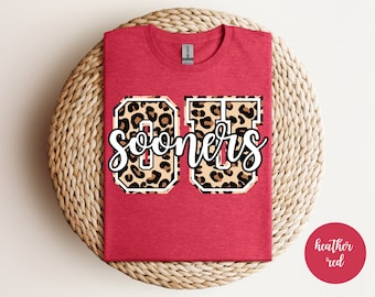 May include: Red t-shirt with a white "OU Sooners" graphic in a leopard print design.