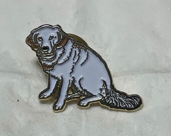 May include: A dog pin featuring a white body, gold trim, and a black tail. The metal pin depicts a Golden Retriever in a sitting position. It has a gold clasp on the back.