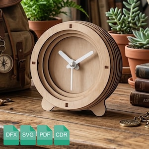 Könnte beinhalten: Eine Holz-Schreibtischuhr mit einem geschichteten Design. Die Uhr hat eine hellbraune Oberfläche, weiße Zeiger und einen kleinen Ständer. Die Uhr ist rund und hat ein minimalistisches Design. Die Uhr hat einen Durchmesser von etwa 13 cm.