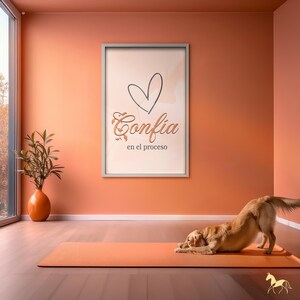 Op de afbeelding: Een oranje yogamat met een golden retriever in de neerwaartse hondhouding. Een ingelijste print op de muur leest "Confia en el proceso" met een hartafbeelding. De kamer heeft oranje muren en een groot raam.