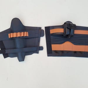 May include: Two pieces of black leather armor with brown accents. One piece has a series of brown cylindrical holders, and the other has a small black pouch. Both pieces have straps for securing.