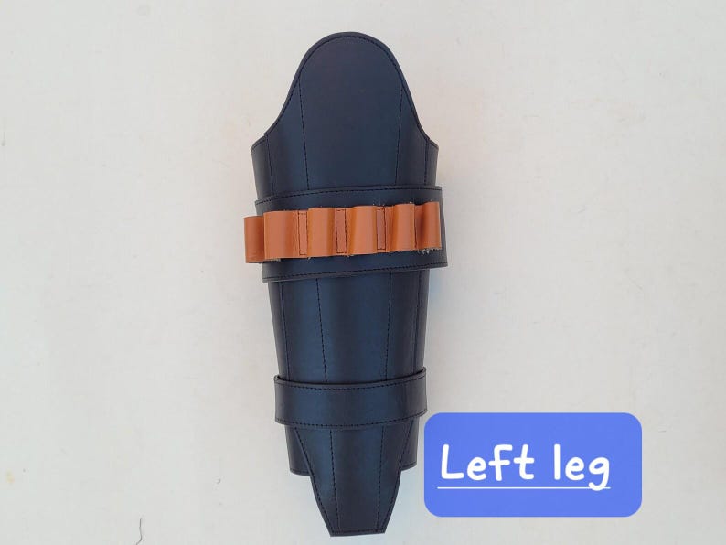 May include: A black leather leg armor with a brown leather band of bullet holders and a strap. The text "Left leg" is in a blue box at the bottom. The armor is designed to protect the leg.