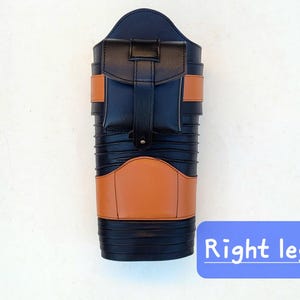 May include: A black and tan leather leg protector with a pocket and straps. The product has a rectangular shape with a rounded top and is labeled "Right leg" in a blue box.