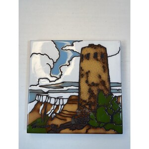 May include: Square ceramic tile featuring a stylized depiction of a desert landscape with a tall, tan tower. The artwork includes a blue sky with white clouds, a canyon, and green foliage. The tile is signed in the lower left corner.