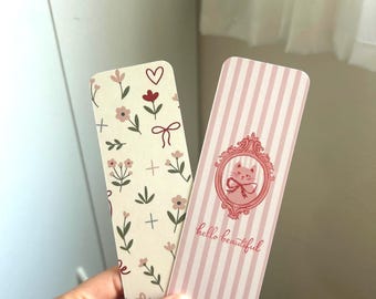 May include: Two decorative bookmarks. One bookmark features a floral pattern with pink flowers, green leaves, and a red heart. The other bookmark has pink stripes and a framed cat illustration with the text "hello beautiful".