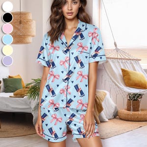 Puede incluir: Conjunto de pijama azul claro con un estampado repetido de lazos rosas, latas de bebidas azul oscuro y peque&ntilde;os corazones negros. El conjunto incluye una camisa abotonada de manga corta y pantalones cortos a juego. El pijama tiene ribetes azul oscuro.