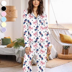 Puede incluir: Conjunto de pijama de sat&eacute;n blanco con un estampado de lazos rosas, corazones azules y latas de Red Bull. La parte superior de manga larga y los pantalones tienen ribetes azul marino. Una c&oacute;moda opci&oacute;n de ropa de dormir.