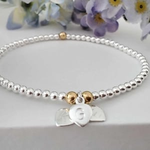 May include: A silver beaded bracelet with two gold beads and a charm with a heart and the letter G.