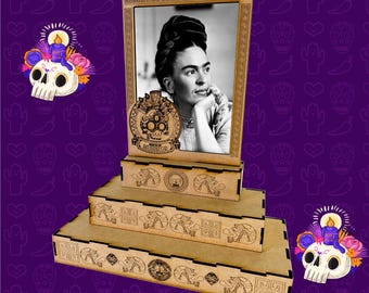 May include: A laser-cut wooden display featuring a black and white portrait of Frida Kahlo. The display has a tiered design with decorative laser-cut patterns and the text "ARCHIVOS DE CORTE LASER" and "ARCHIVOS SVG. PDF. AI". The background is purple with Day of the Dead themed illustrations.