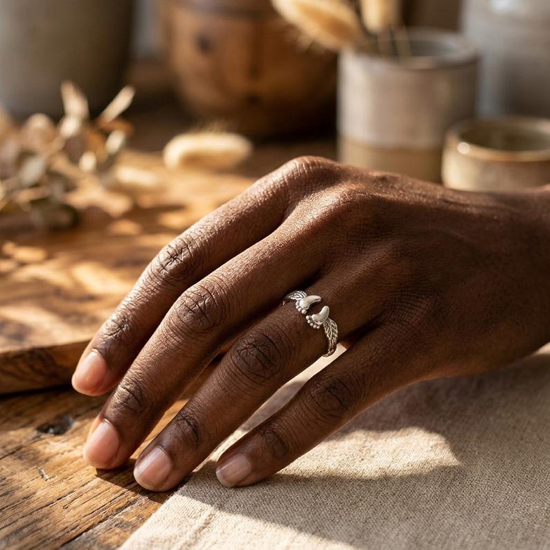 May include: A silver ring featuring a detailed design of two open wings. The ring is worn on a finger, showcasing the intricate details of the wings and the band. The ring is a piece of jewelry.