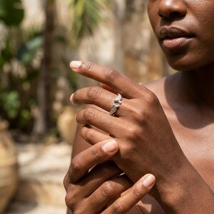 May include: A silver ring with a detailed design featuring two stylized bird wings. The ring is worn on a finger, showcasing its intricate craftsmanship and elegant aesthetic. The ring's design is visible against the skin.