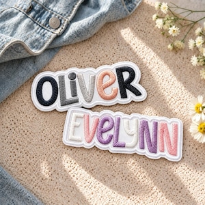 Puede incluir: Dos parches bordados personalizados con fondo de tela blanca y bordes festoneados. El parche superior muestra el nombre OLIVER en hilo azul oscuro, gris y melocotón. El parche inferior muestra el nombre EVELYNN en hilo blanco, rosa y morado.