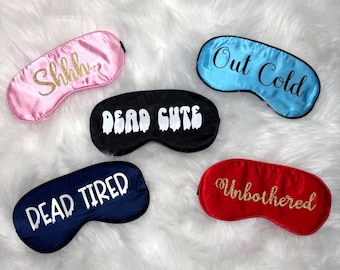 May include: Five satin sleep masks in different colours. They include a pink mask with gold glitter text "Shhh..", a blue mask with "Out Cold", a black mask with "Dead Cute", a navy mask with "Dead Tired", and a red mask with "Unbothered".