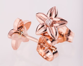 May include: A pair of rose gold earrings featuring a delicate flower design with a small diamond in the center. The earrings have a post and butterfly back closure.