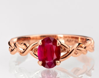 May include: A rose gold ring with a braided band and a large oval ruby gemstone.