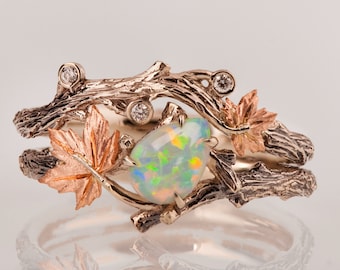 May include: A delicate ring featuring a pear-shaped opal set in a branch-like design with two small diamonds and two maple leaves. The ring is made of gold and has a rustic, nature-inspired aesthetic.